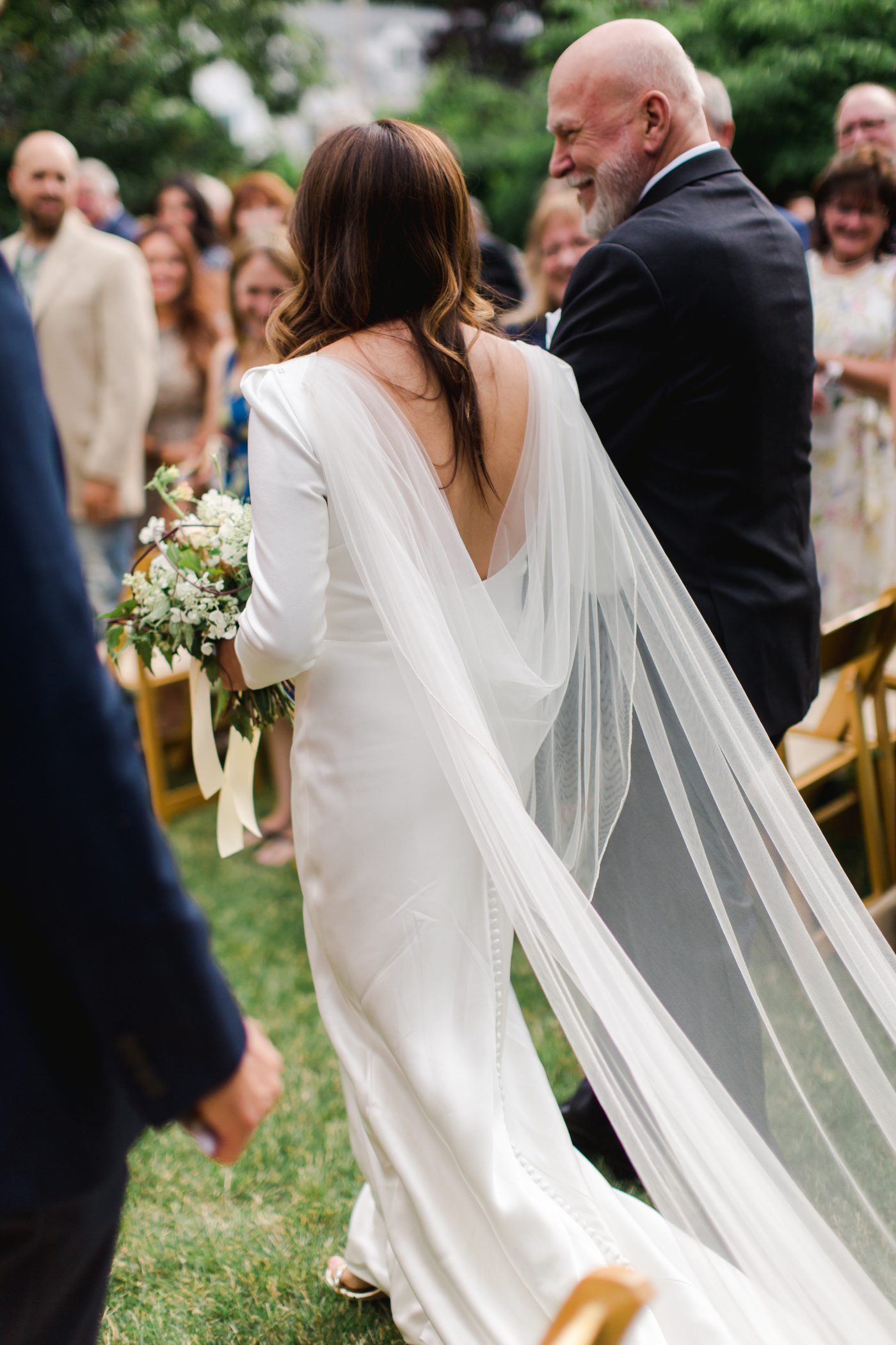Bride walking down the aisle with her tulle cape flowing behind