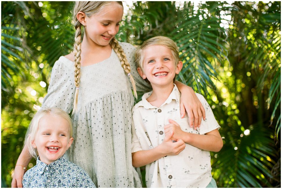 Three blond children smiling together with greenery in the background in Naples Florida