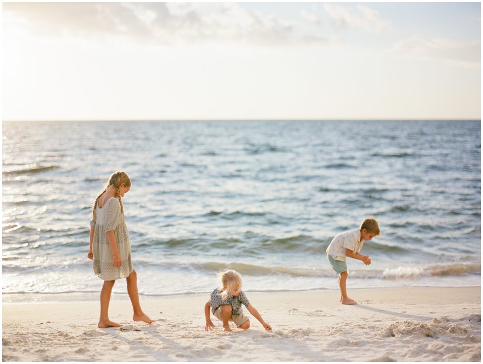 three children playing in the sand on the beach in Naples Florida while on vacation with the water behind them